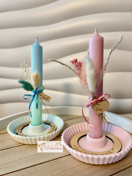 Zwei dekorative Kerzen in Farbtönen Blau und Rosa auf Tellern mit floralen Akzenten.